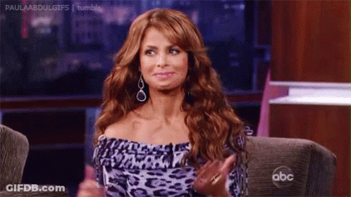 A Woman With Red Hair Is Sitting On A Couch With Her Hands In The Air . GIF