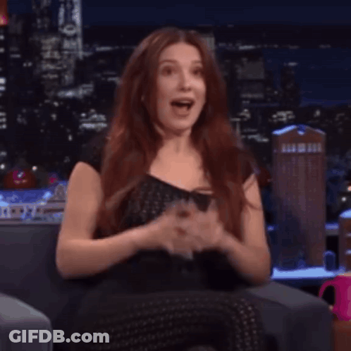 A Woman With Red Hair Is Sitting On A Couch With Her Mouth Open And Making A Funny Face . GIF