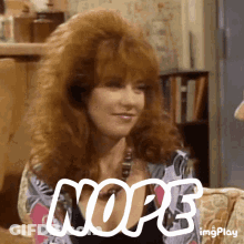 A Woman With Red Hair Is Sitting On A Couch With The Word Nope Written In White Letters . GIF
