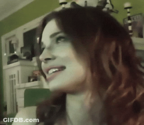 A Woman With Red Hair Is Smiling And Looking To The Side GIF