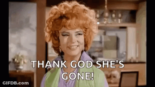 A Woman With Red Hair Is Smiling And Saying `` Thank God She 'S Gone '' In A Kitchen . GIF