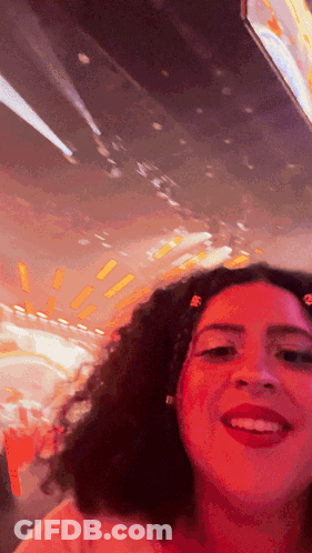 A Woman With Red Hair Is Smiling In Front Of A Blurred Background GIF