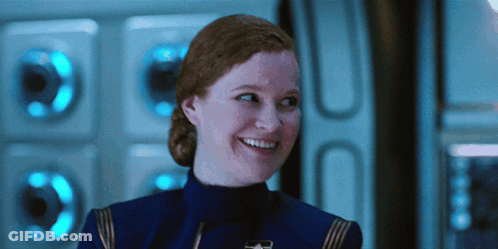 A Woman With Red Hair Is Smiling In Front Of A Wall With Blue Lights GIF