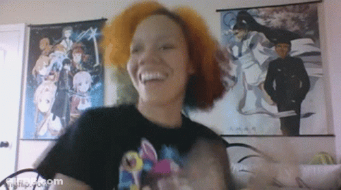 A Woman With Red Hair Is Smiling In Front Of Anime Posters On The Wall GIF