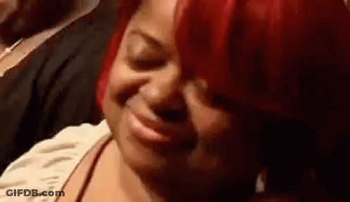 A Woman With Red Hair Is Smiling While Sitting In A Crowd Of People . GIF