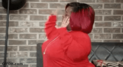 A Woman With Red Hair Is Standing In Front Of A Brick Wall And Covering Her Face With Her Hands . GIF