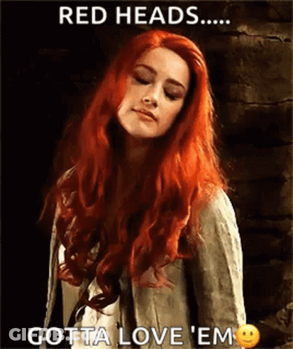 A Woman With Red Hair Is Standing In Front Of A Brick Wall With Her Eyes Closed . GIF
