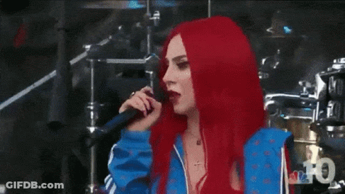 A Woman With Red Hair Is Standing In Front Of A Drum Set And Looking At The Camera . GIF