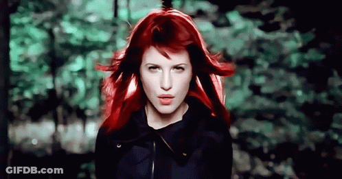 A Woman With Red Hair Is Standing In Front Of A Forest GIF