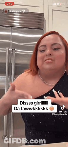 A Woman With Red Hair Is Standing In Front Of A Stainless Steel Refrigerator And Has A Tiktok App Open GIF