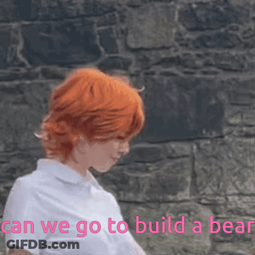 A Woman With Red Hair Is Standing In Front Of A Stone Wall With The Words " Can We Go To Build A Bear " Above Her GIF