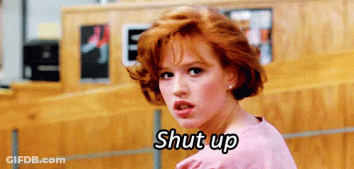 A Woman With Red Hair Is Standing In Front Of A Wooden Wall And Saying Shut Up . GIF
