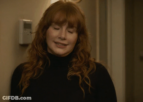A Woman With Red Hair Is Waving Her Hand In Front Of A Door GIF