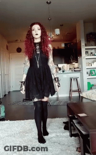 A Woman With Red Hair Is Wearing A Black Dress And Black Socks GIF