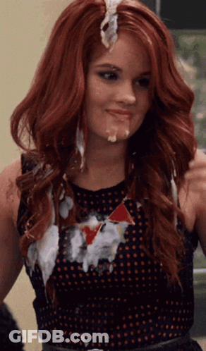 A Woman With Red Hair Is Wearing A Black Polka Dot Dress And Has A Lot Of White Icing On Her Face . GIF