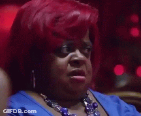 A Woman With Red Hair Is Wearing A Blue Dress And A Blue Necklace And Making A Funny Face . GIF