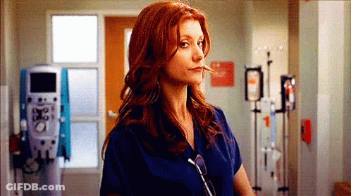 A Woman With Red Hair Is Wearing A Blue Scrub Top And Sunglasses In A Hospital Hallway . GIF