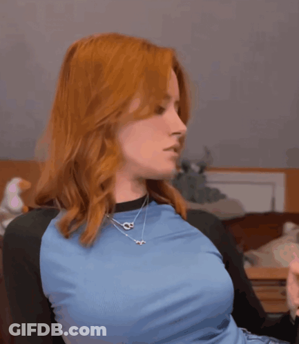 A Woman With Red Hair Is Wearing A Blue Shirt And Necklaces GIF