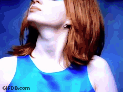 A Woman With Red Hair Is Wearing A Blue Tank Top And Earrings GIF