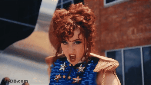 A Woman With Red Hair Is Wearing A Blue Top With Gold Stars GIF