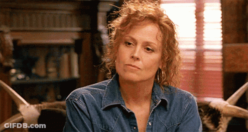 A Woman With Red Hair Is Wearing A Denim Shirt And Earrings GIF