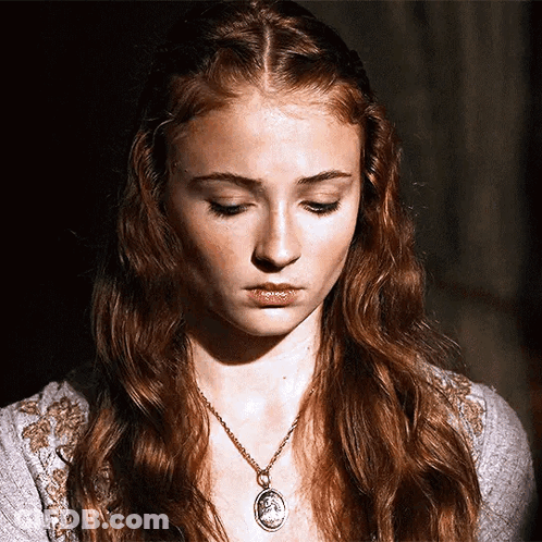 A Woman With Red Hair Is Wearing A Necklace With A Medallion On It GIF