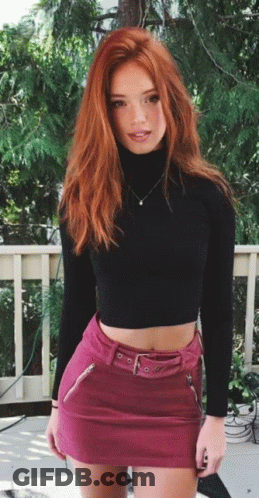 A Woman With Red Hair Is Wearing A Pink Skirt And A Black Turtleneck GIF