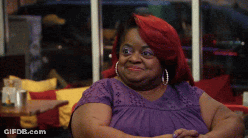 A Woman With Red Hair Is Wearing A Purple Shirt And Pearl Earrings GIF