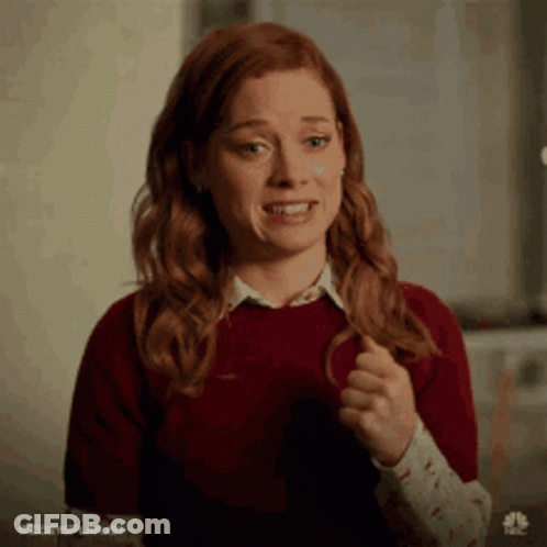 A Woman With Red Hair Is Wearing A Red Sweater And A White Shirt And Is Making A Funny Face . GIF