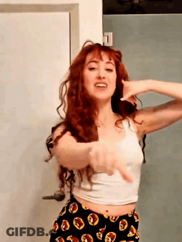 A Woman With Red Hair Is Wearing A White Tank Top And Black Pants GIF
