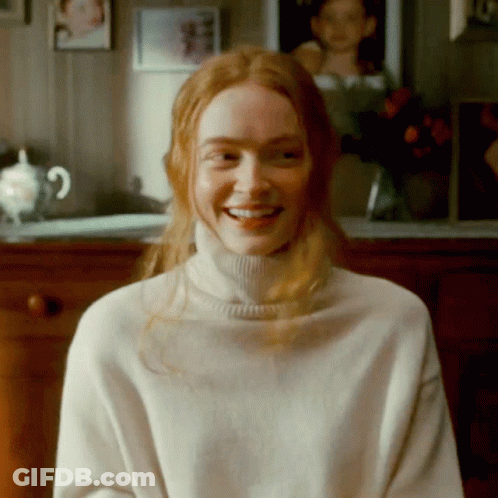 A Woman With Red Hair Is Wearing A White Turtleneck And Smiling GIF
