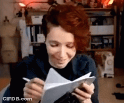 A Woman With Red Hair Is Writing On A Piece Of Paper While Holding A Pen . GIF