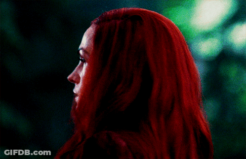 A Woman With Red Hair Looks At The Camera With A Green Background GIF