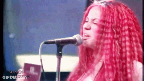 A Woman With Red Hair Singing Into A Microphone With The Words Somos Shakifans Written On The Bottom GIF