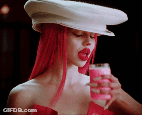 A Woman With Red Hair Wearing A White Hat And Holding A Glass Of Pink Liquid GIF
