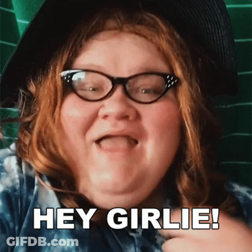 A Woman With Red Hair Wearing Glasses And A Hat Says Hey Girlie GIF