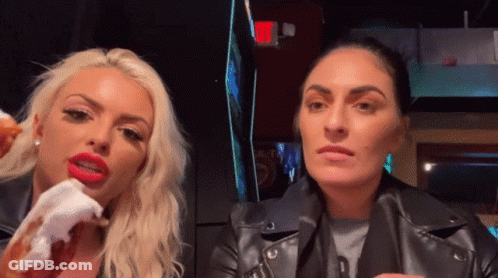 A Woman With Red Lips Is Eating A Donut Next To Another Woman In A Black Leather Jacket GIF
