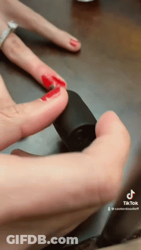 A Woman With Red Nails Is Holding A Bottle Of Nail Polish In Her Hand GIF