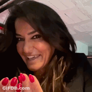 A Woman With Red Nails Is Smiling And Looking At The Camera . GIF