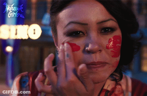 A Woman With Red Paint On Her Face Has A Sign Behind Her That Says Soho GIF