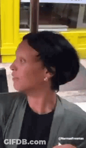 A Woman With Short Black Hair Is Sitting In Front Of A Yellow Door . GIF