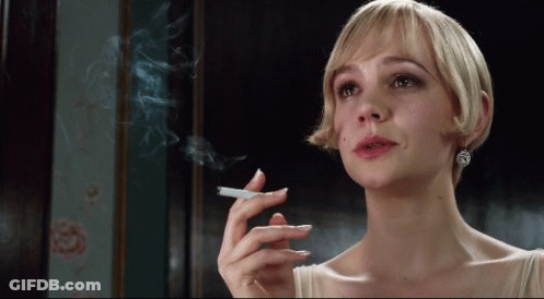 A Woman With Short Blonde Hair Is Smoking A Cigarette In A Dark Room GIF