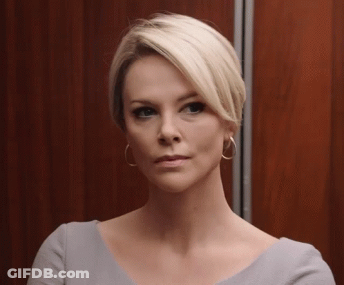 A Woman With Short Blonde Hair Wearing Hoop Earrings Looks At The Camera GIF