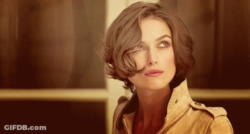 A Woman With Short Brown Hair Is Wearing A Brown Jacket And Looking Up . GIF