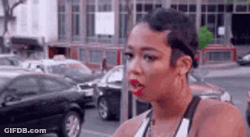 A Woman With Short Hair And Red Lipstick Is Standing On A Street In Front Of A Parking Meter . GIF