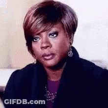 A Woman With Short Hair Is Making A Funny Face While Wearing A Black Jacket And Earrings . GIF
