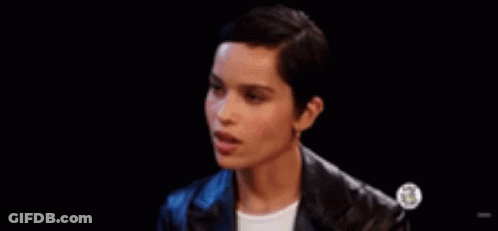 A Woman With Short Hair Is Wearing A Leather Jacket And Earrings And Making A Funny Face . GIF