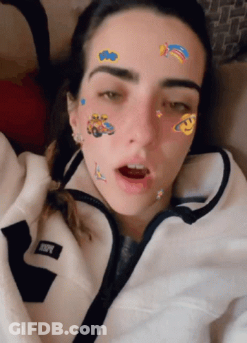 A Woman With Stickers On Her Face Is Wearing A White Jacket With The Letter R On The Front GIF