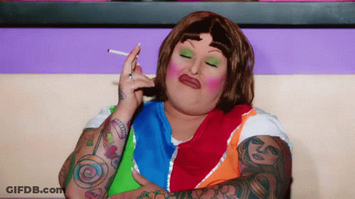 A Woman With Tattoos On Her Arms Is Smoking A Cigarette While Wearing A Colorful Shirt GIF