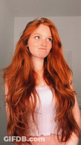 A Woman With Very Long Red Hair Is Wearing A White Top GIF